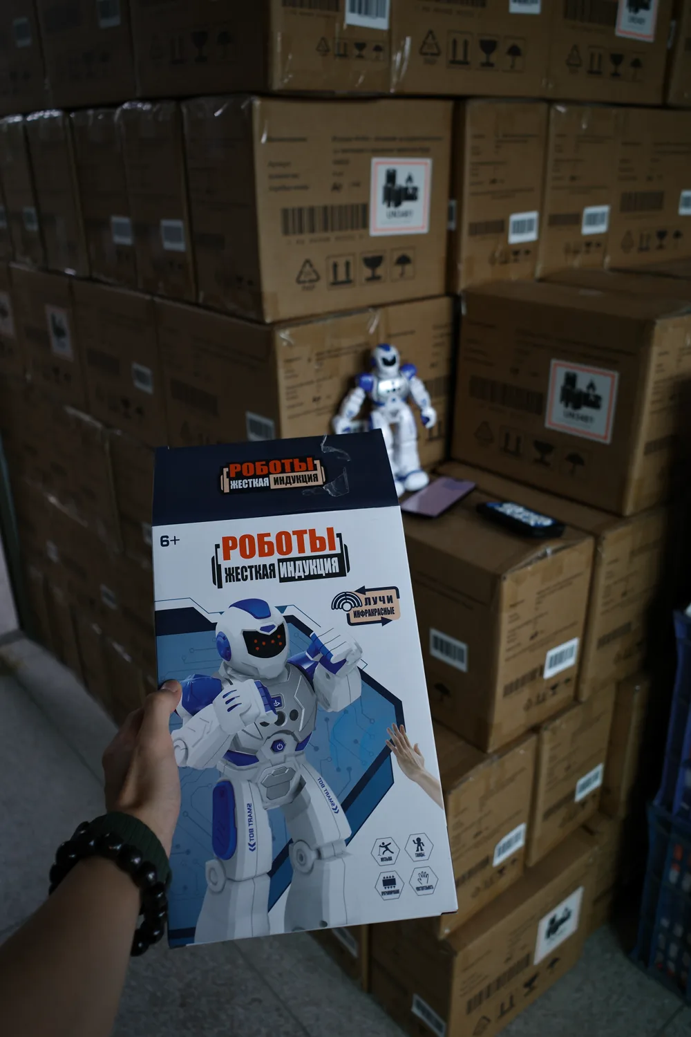 A retail package held in front of stacked shipping cartons